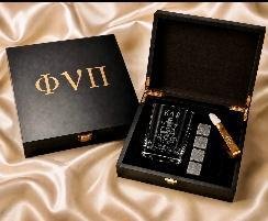 Black gift box lid embossed Phi Nu Pi beside an open box holding an engraved glass, whiskey stones and tongs