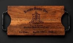 Wood serving board with black iron handles engraved with a Kappa Alpha Psi crest and chapter text